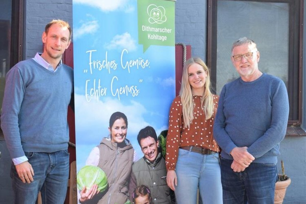 3 Personen stehen neben einem Plakat auf dem eine Familie mit Kohlköpfen zu sehen ist